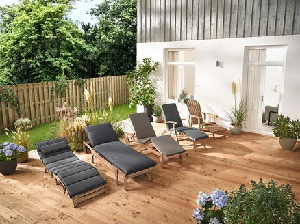 Na dřevěné terase stojí několik zahradních lehátek a zahradní křeslo Adirondack s výsuvnou podnožkou z dřeva.