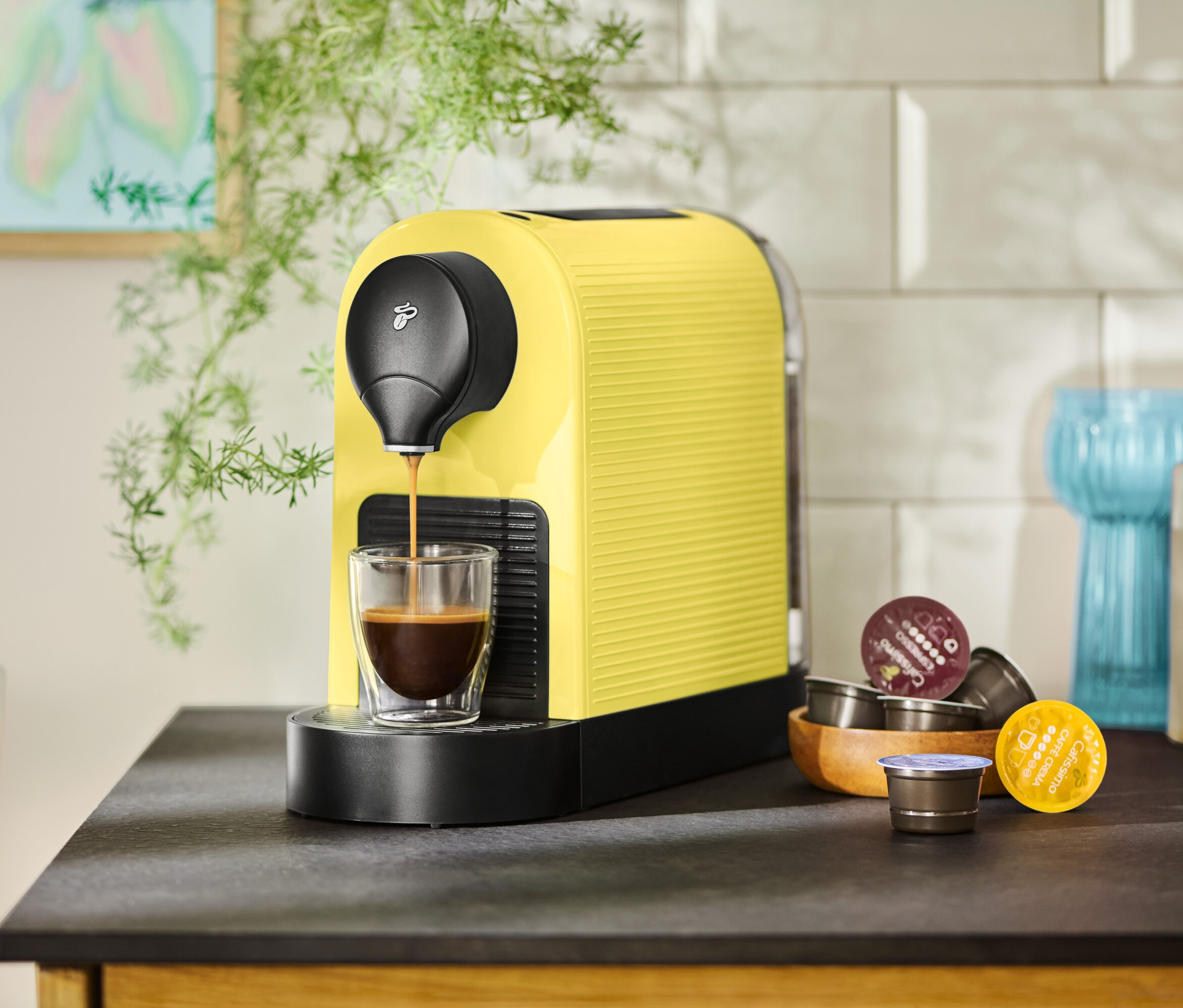 Žlutý kávovar plní šálek kávou, vedle leží kapsle.