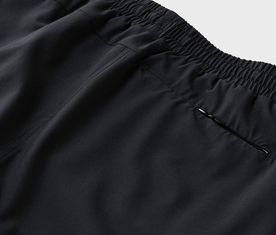 Detailní záběr zadní části černých kalhot s elastickým pasem a kapsou na zip.