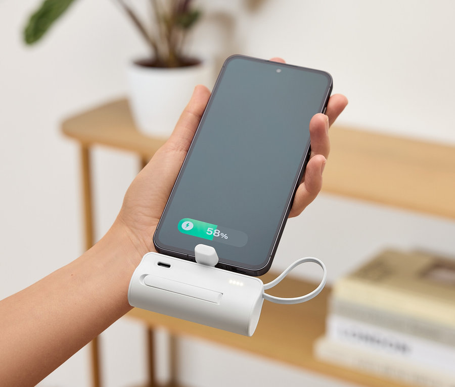 Ruka drží smartphone připojený k bílé přenosné nabíječce. Úroveň nabití baterie telefonu je 58 %.
