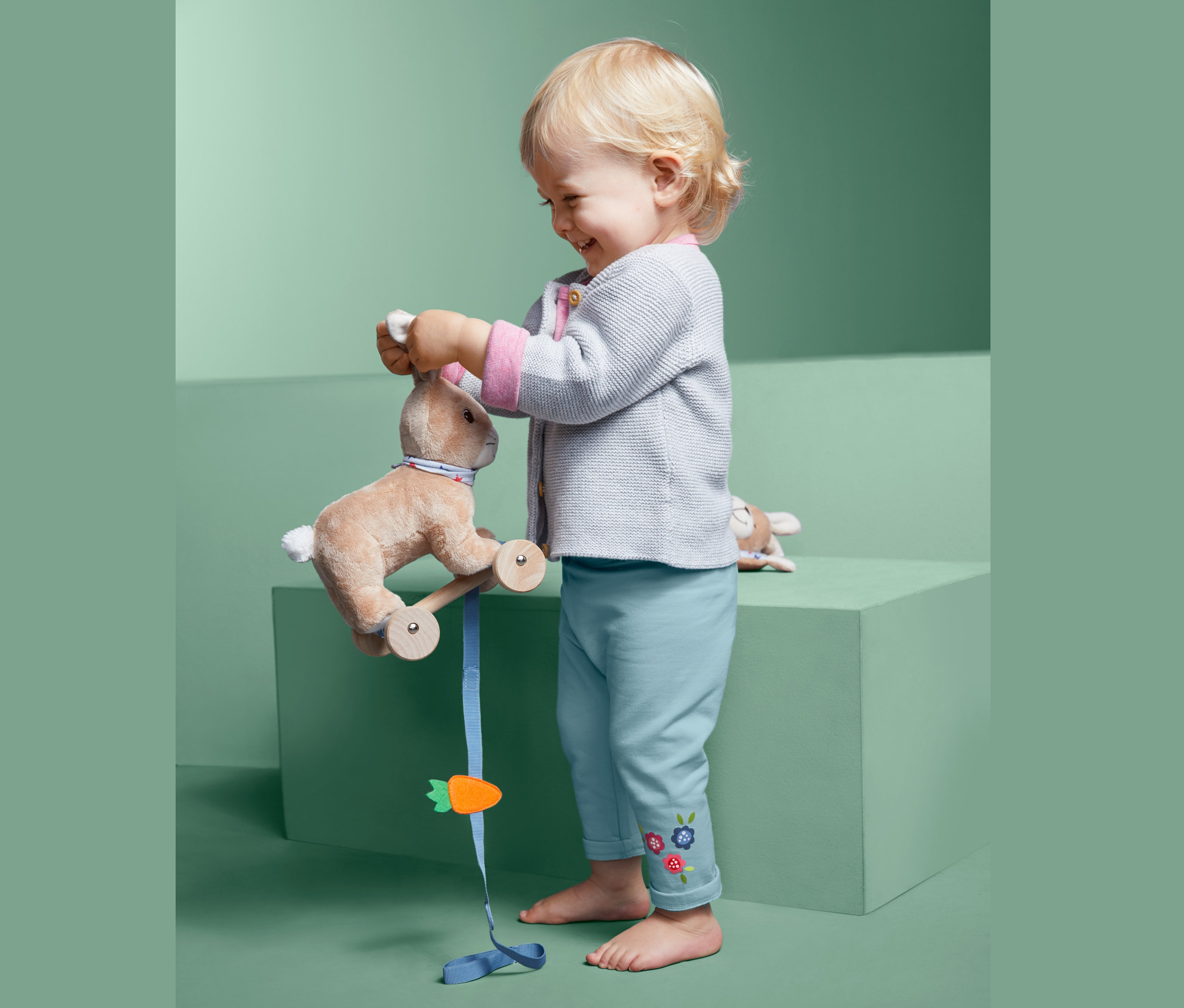 Batole si hraje s plyšovým králíkem na kolečkách a má na sobě teplákové kalhoty.