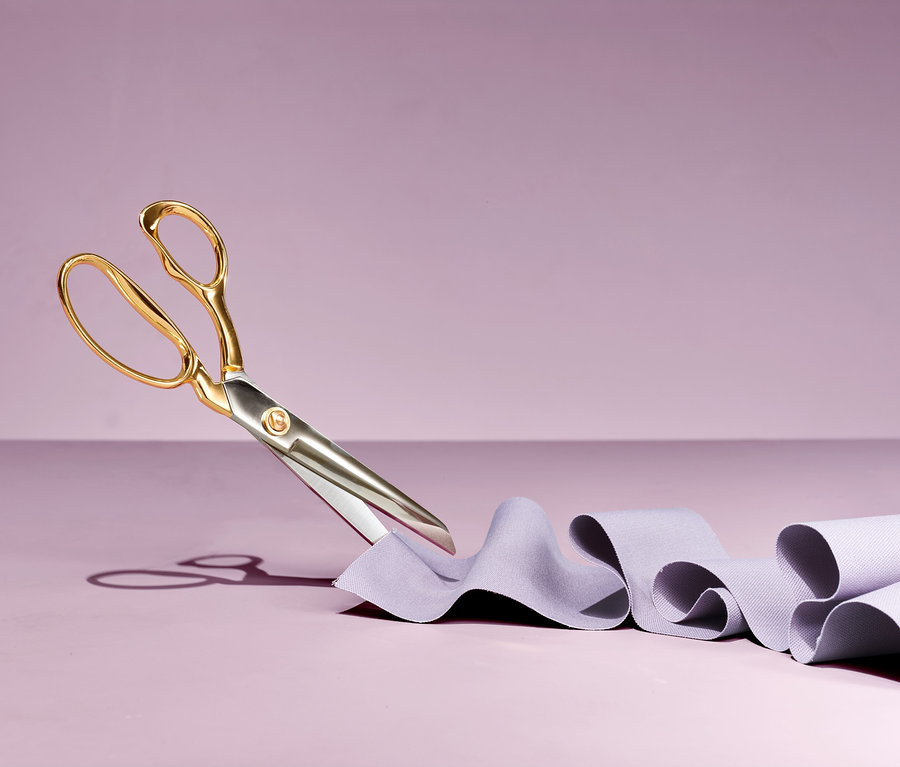 Profesionální krejčovské nůžky stříhají fialovou látku na fialovém pozadí.