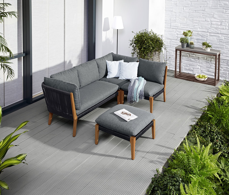 Rohová sedací souprava s podnožkou na terase s LED venkovní stojací lampou v pozadí.