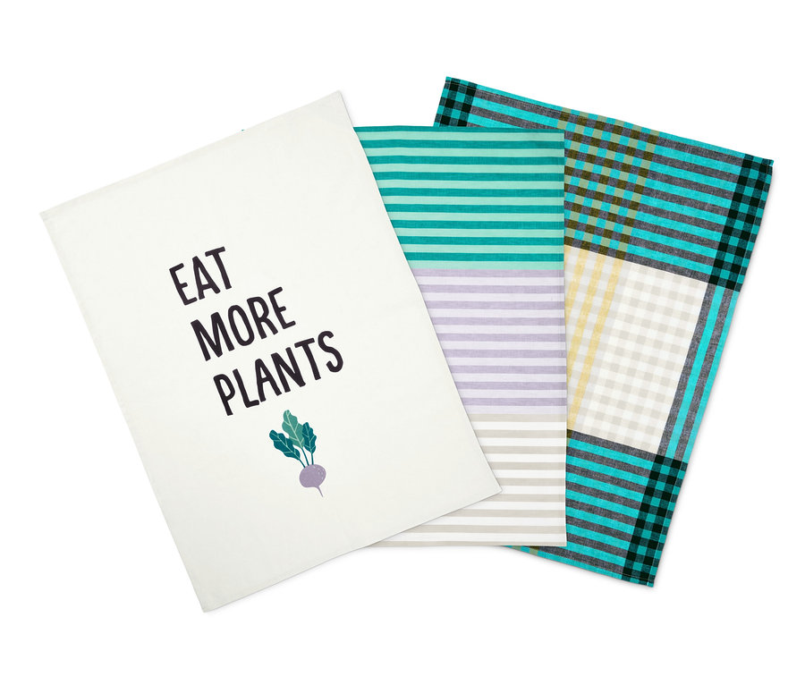 Tři utěrky na nádobí: bílá s nápisem "Jezte více rostlin", pruhovaná a kostkovaná.