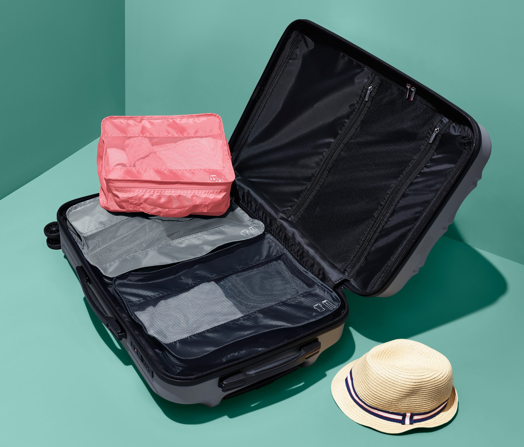 Otevřený kufr s cestovními organizéry, 3 ks, a klobouk.