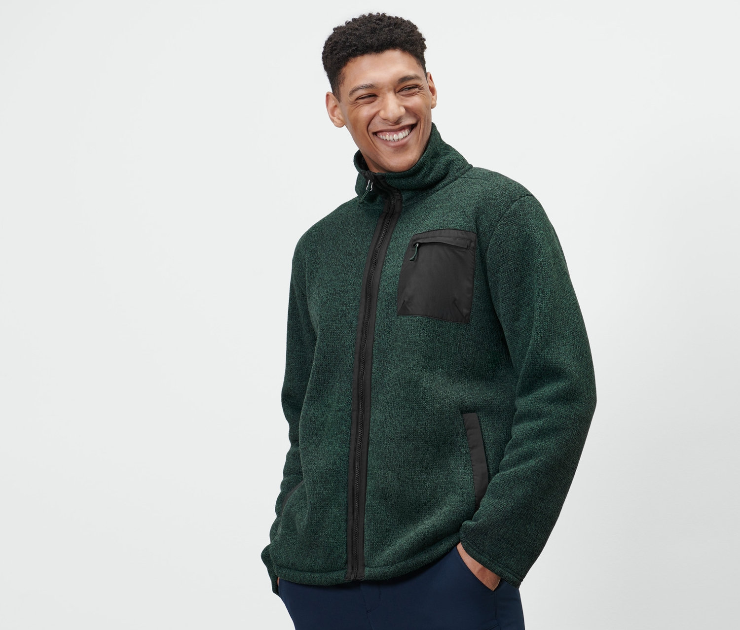 Muž má na sobě zelenou termobundu z pleteného fleecu a tmavě modré kalhoty.