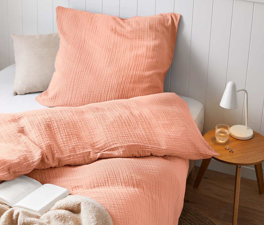 Mušelínové povlečení standardní a nadměrné velikosti na posteli s knihou a lampou.