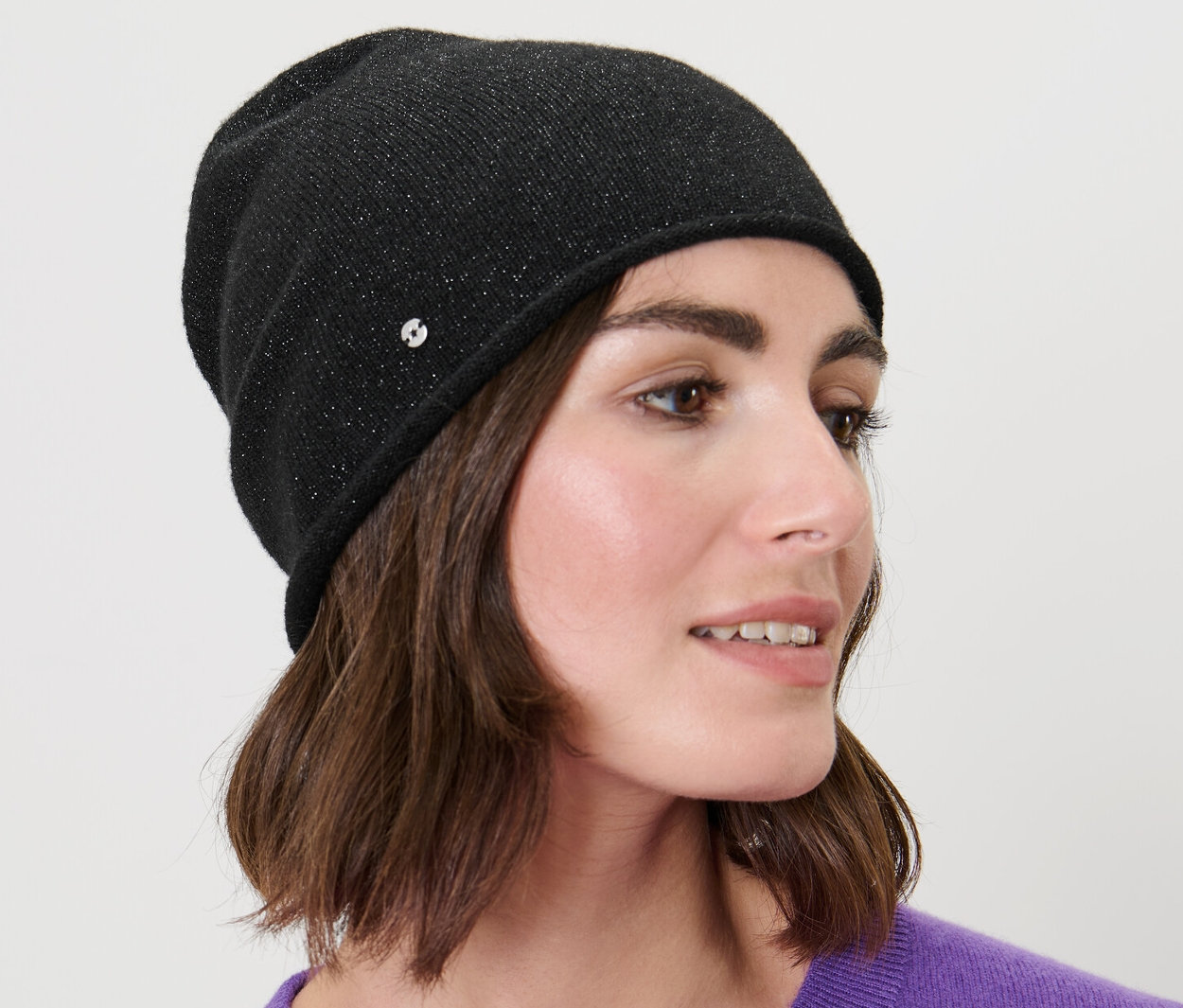 Žena s hnědými vlasy nosí černou třpytivou čepici beanie z jemného úpletu.