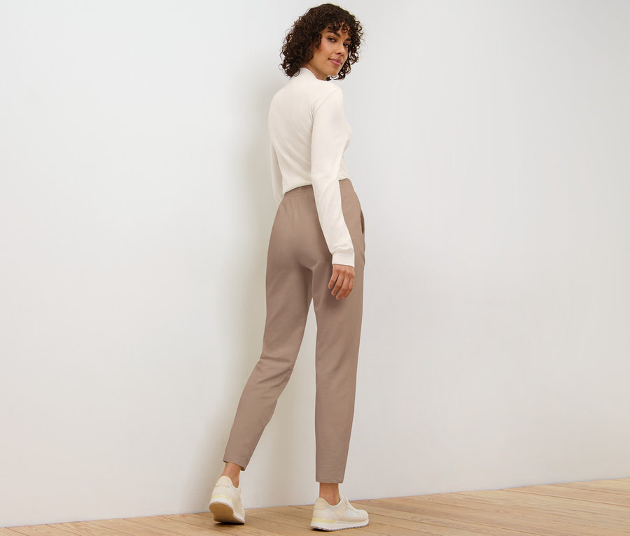 Žena se dívá přes rameno a má na sobě béžové kalhoty joggpant.