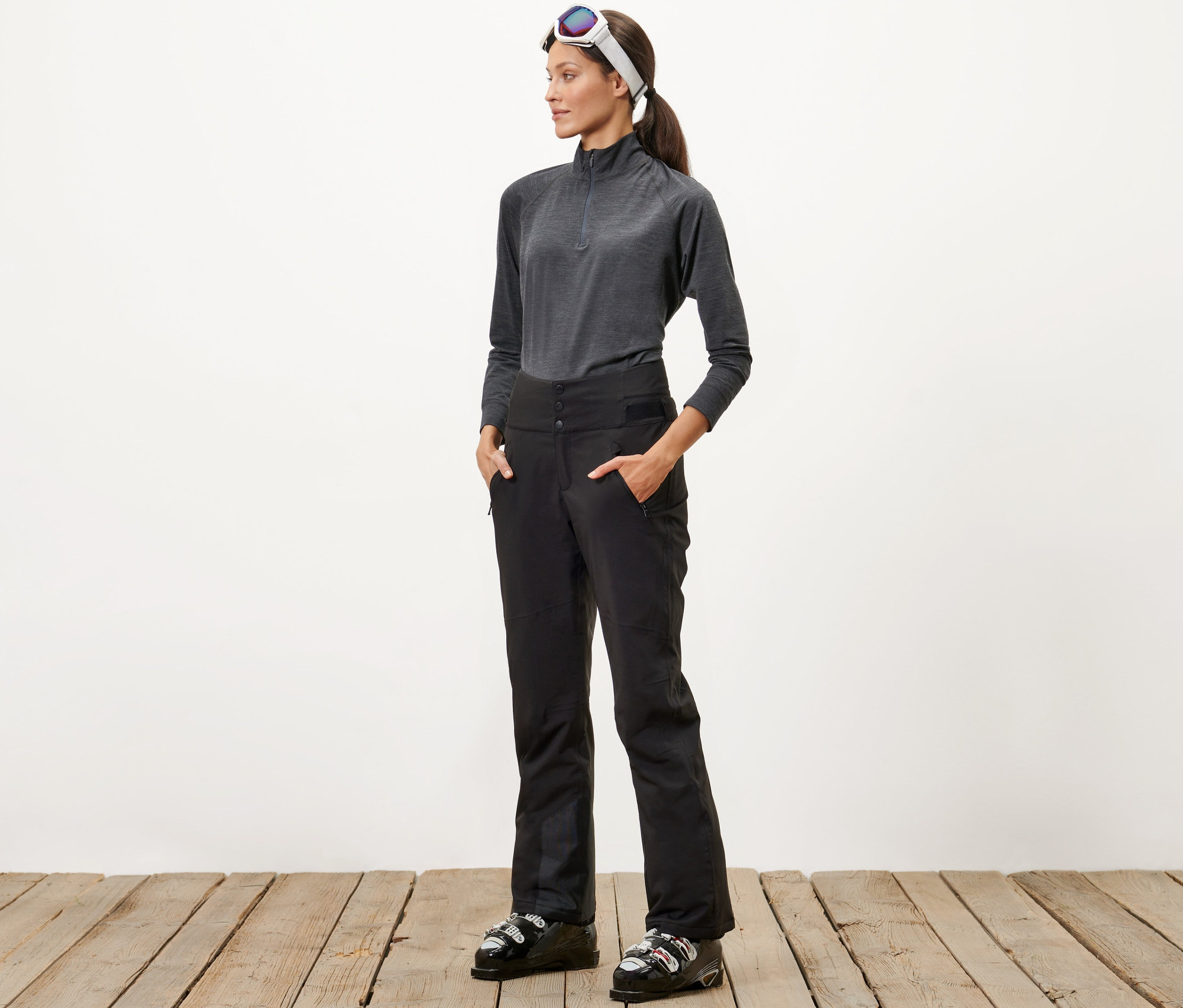 Žena stojí a má ruce v kapsách lyžařských kalhot s vysokým pasem.