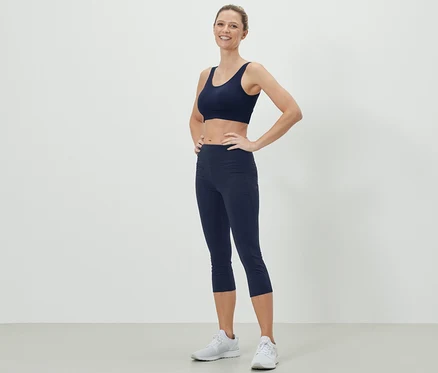 Žena pózuje v tmavě modré sportovní podprsence a 3/4 sportovních legínách.