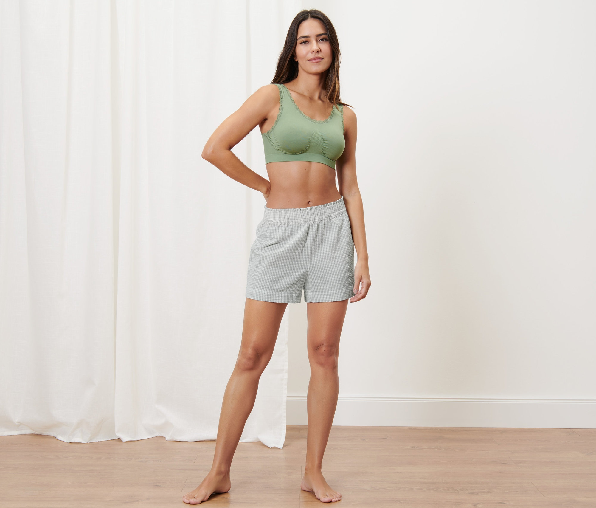 Žena stojí a pózuje v zelené sportovní podprsence a tkaných šortkách.