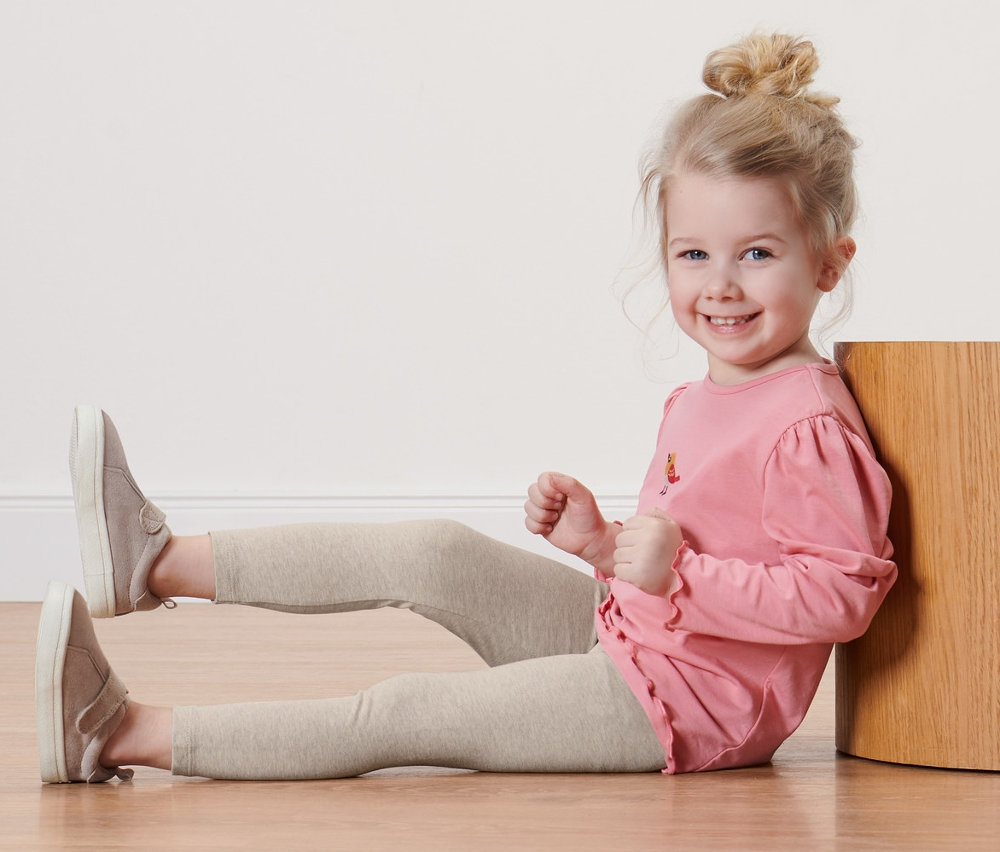 Usmívající se dívka sedí na podlaze v jednobarevných legínách.