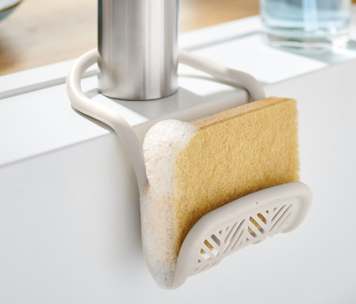 Držák na houbičku s houbičkou upevněný na kohoutku v bílém dřezu.