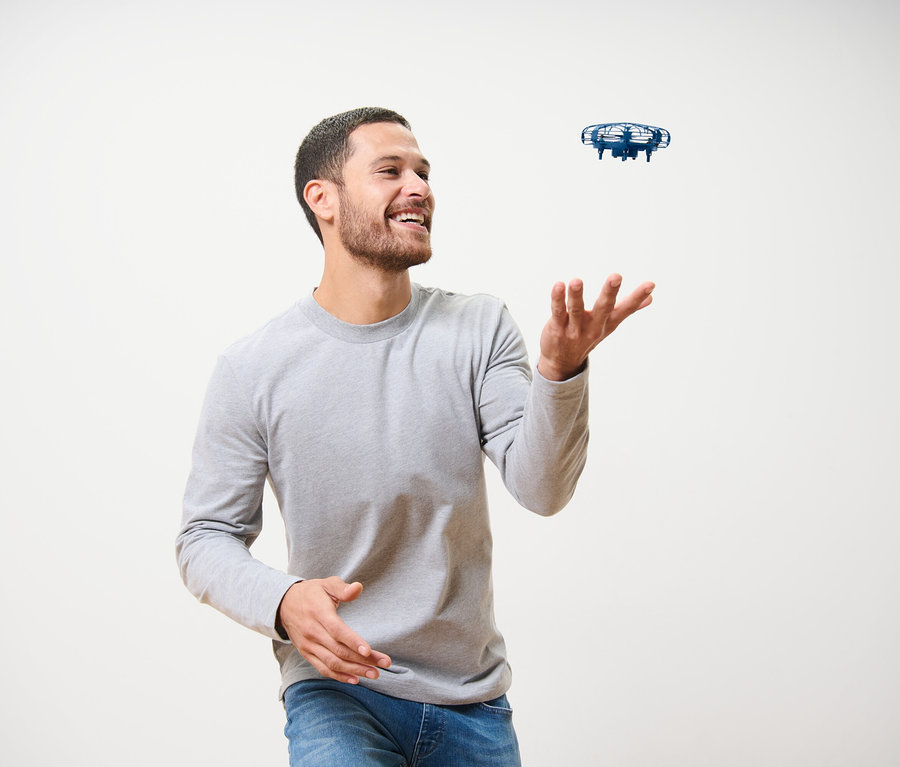 Muž se směje a hraje si s modrým minidronem »UFO«.