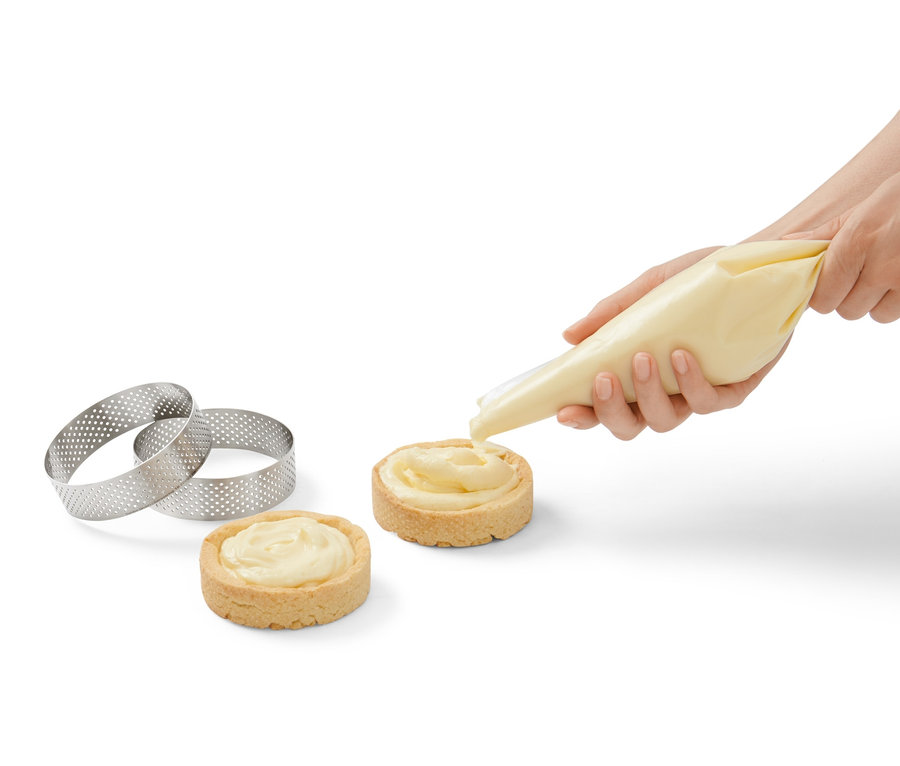 Žena zdobí krémem dva koláče. Vedle leží dva ráfky na pečení z ušlechtilé oceli, 4 ks.