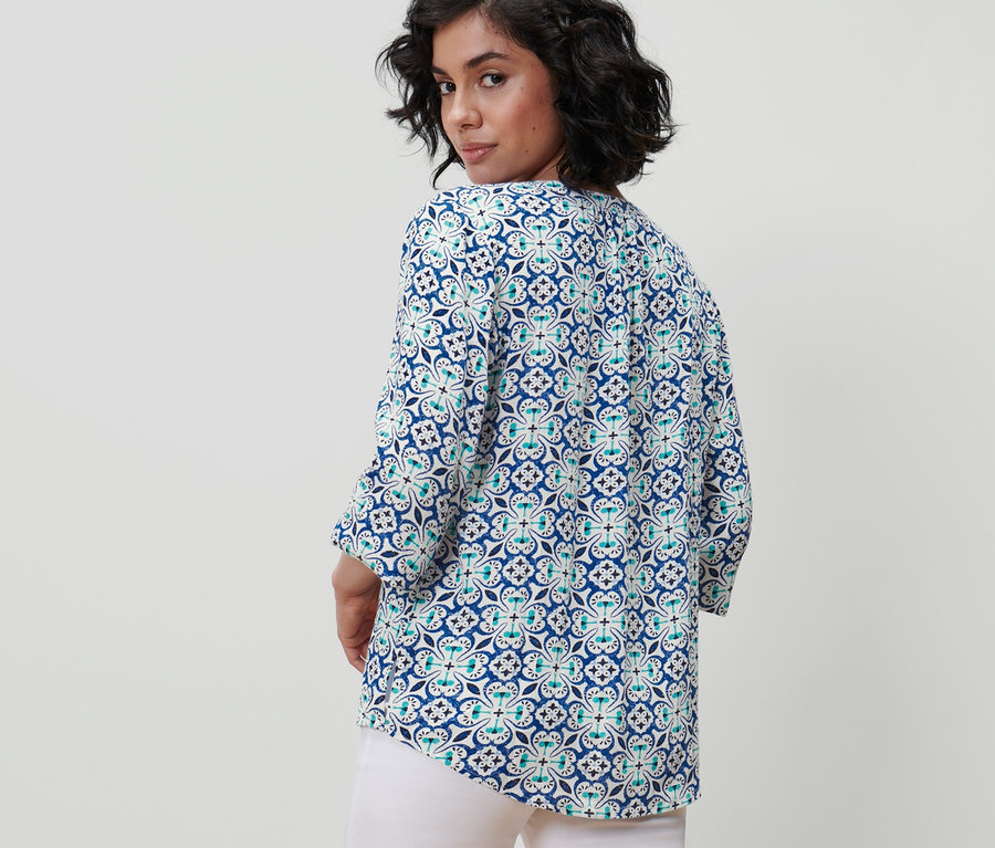 Žena se dívá přes rameno a má na sobě tunikovou halenku s celoplošným potiskem.