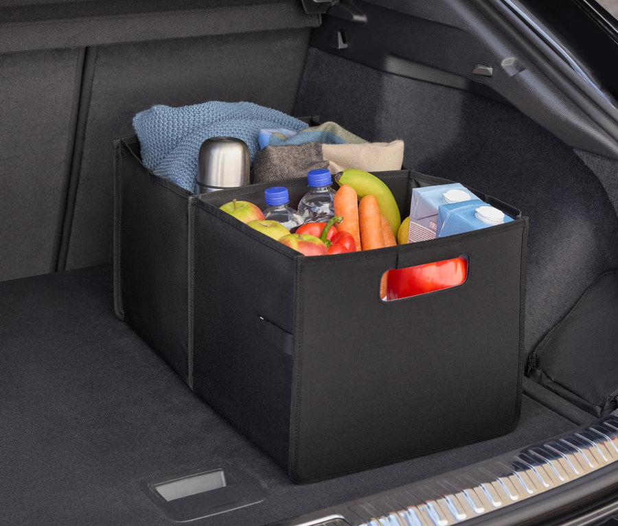 V kufru auta je černý organizér plný potravin, lahví s vodou, ovoce a zeleniny.