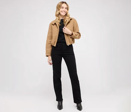 Žena pózuje v džínách Angels »Lara« straight fit, černém topu a hnědé bundě.