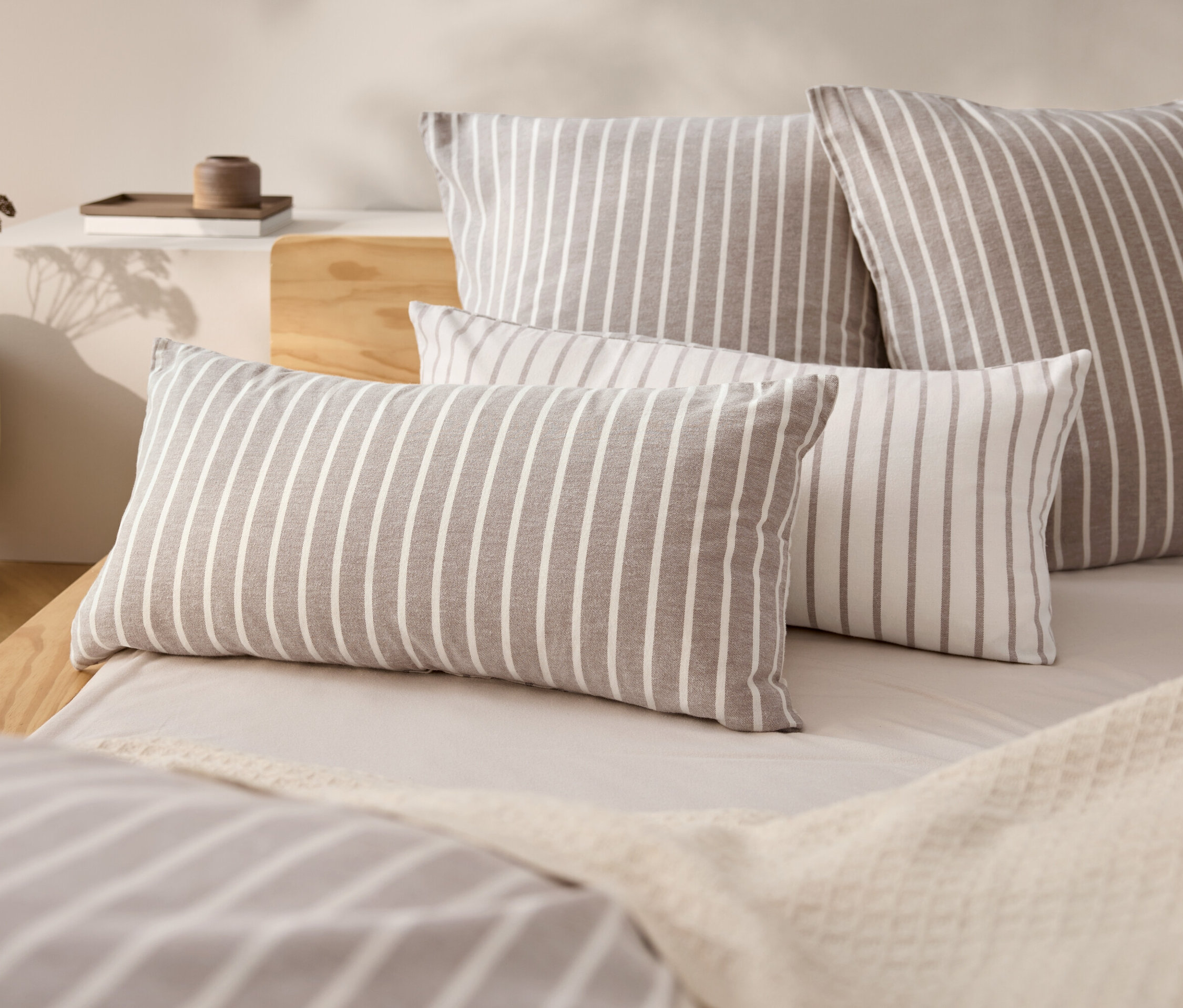 Čtyři pruhované polštáře na posteli s béžovým přehozem.