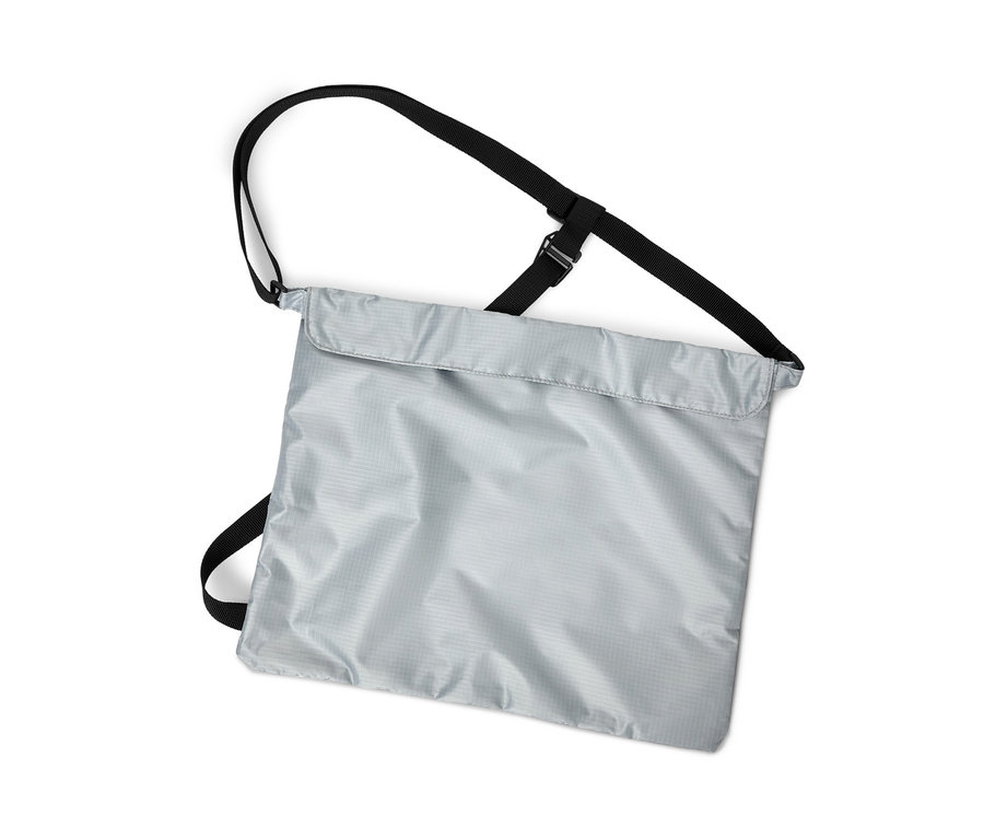 Svisle orientovaná fotografie nákupní tašky na kolo stříbrné barvy s černými popruhy na bílém pozadí.