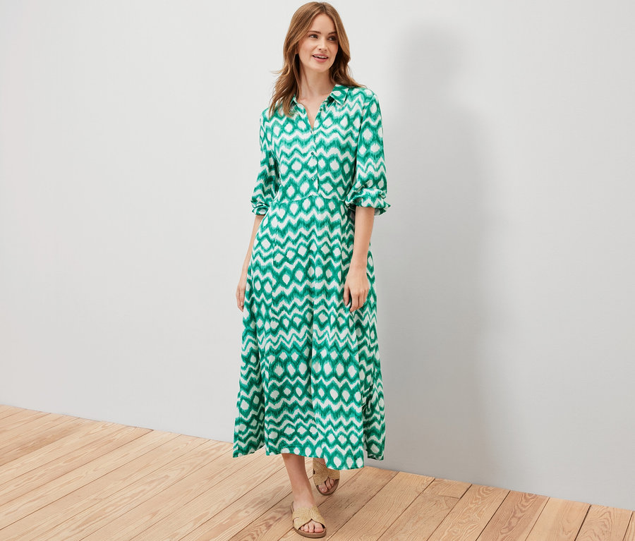 Žena pózuje v zelených vzorovaných košilových šatech.