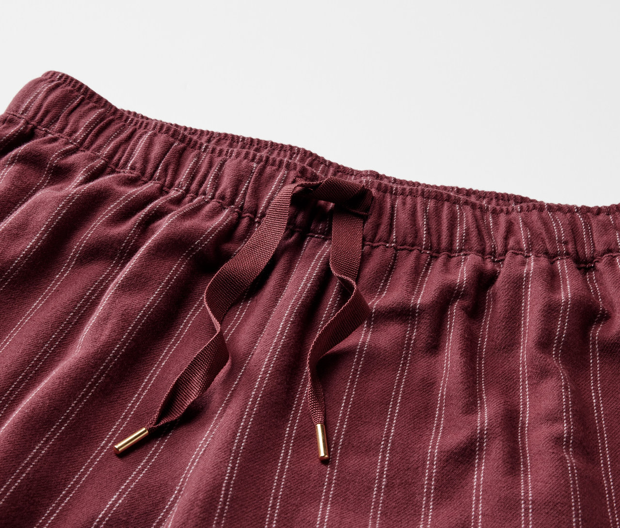 Detail bordó pruhovaných kalhot s elastickým pasem a stahovací šňůrkou.