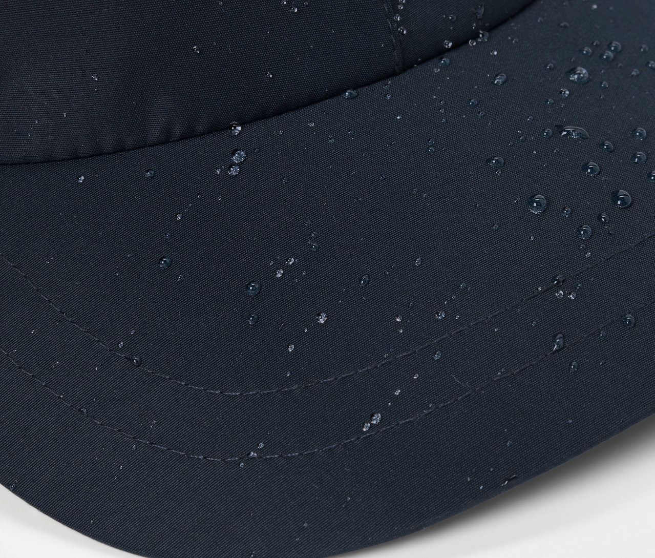 Detailní záběr černé čepice do každého počasí s kapkami vody na povrchu.