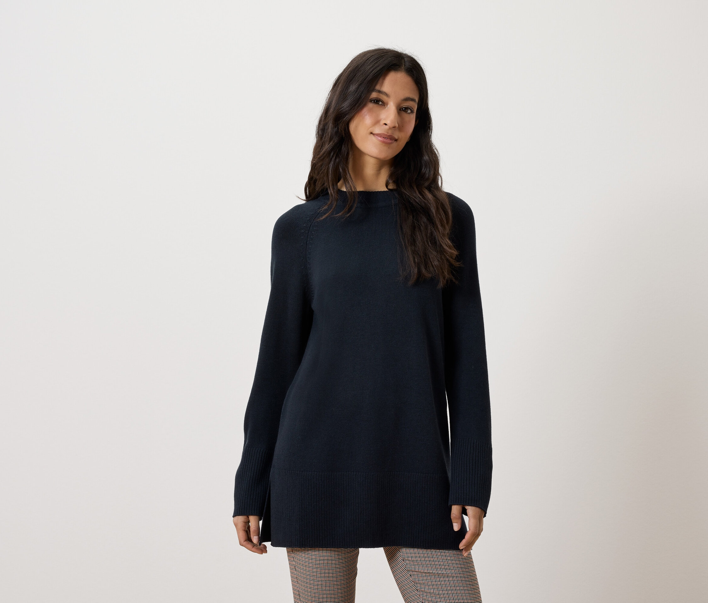 Žena má na sobě dlouhý tmavě modrý svetr a hnědé kalhoty.