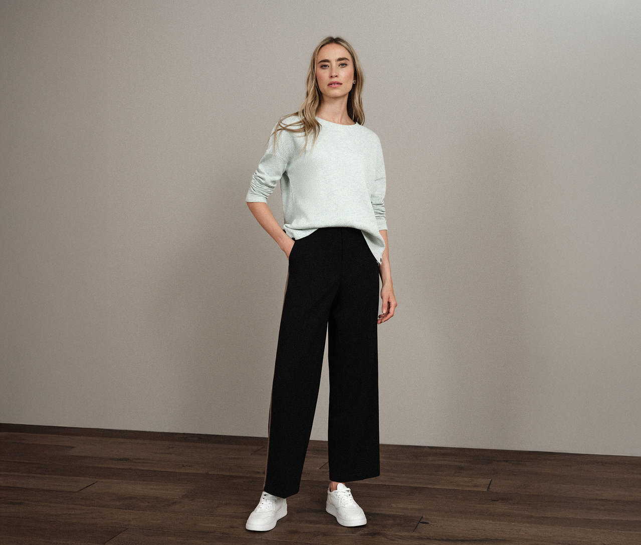 Žena stojí s rukou v kapse a má na sobě strukturované tričko Street One, černé kalhoty a bílé tenisky.