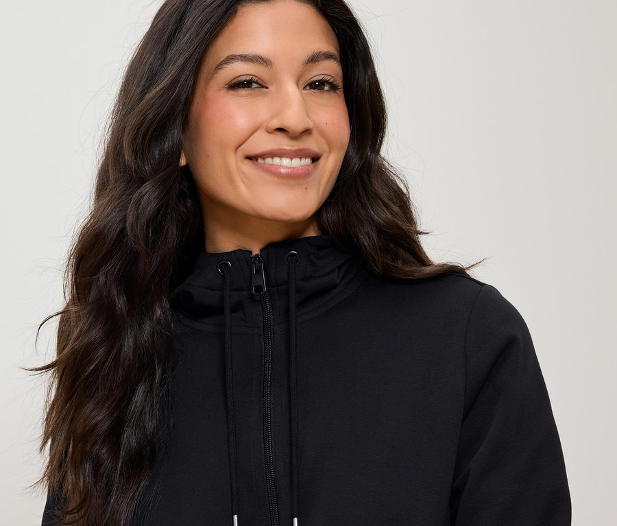 Portrét ženy s dlouhými hnědými vlasy, která má na sobě černou mikinu na zip.