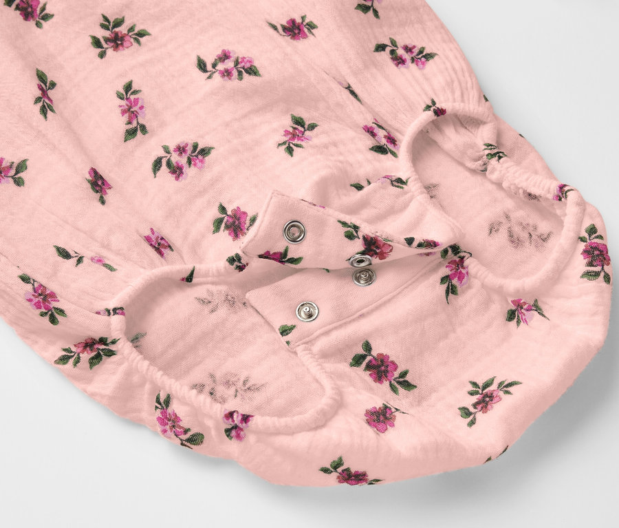 Detail mušelínového body pro miminka s květinovým vzorem a zapínáním na patentky.