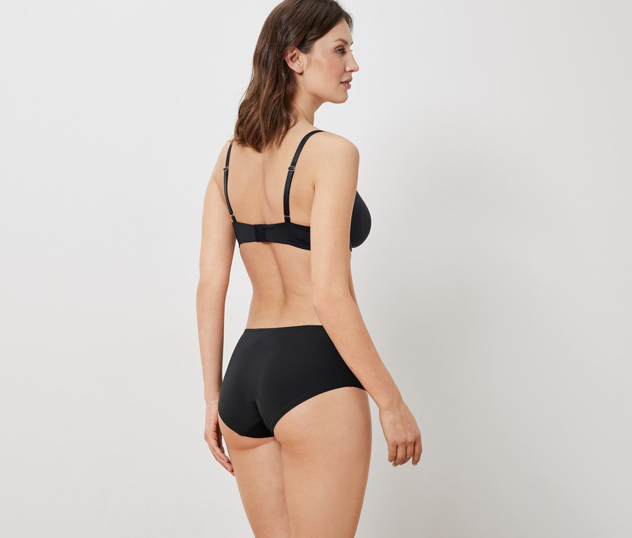 Žena zády k fotoaparátu má na sobě černou podprsenku a kalhotky.