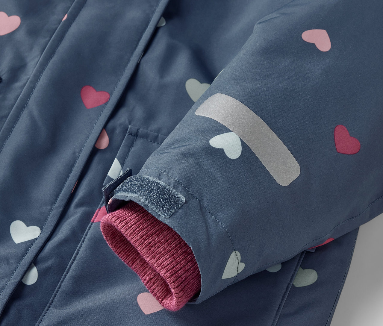 Detail modré 2dílné dětské zimní kombinézy s růžovými a bílými srdíčky.