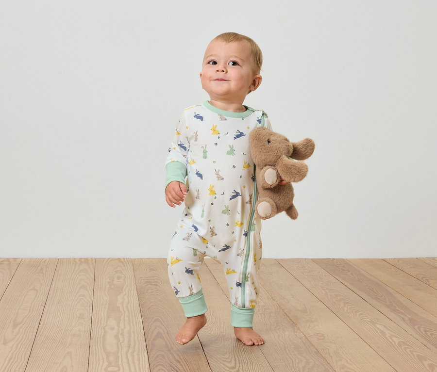 Dítě stojí na dřevěné podlaze a drží plyšového slona.