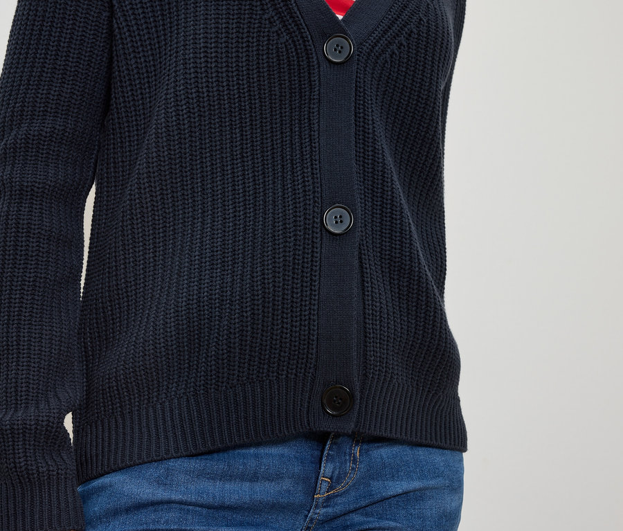 Torzo osoby v modrém pleteném svetru na knoflíky a modrých džínách.