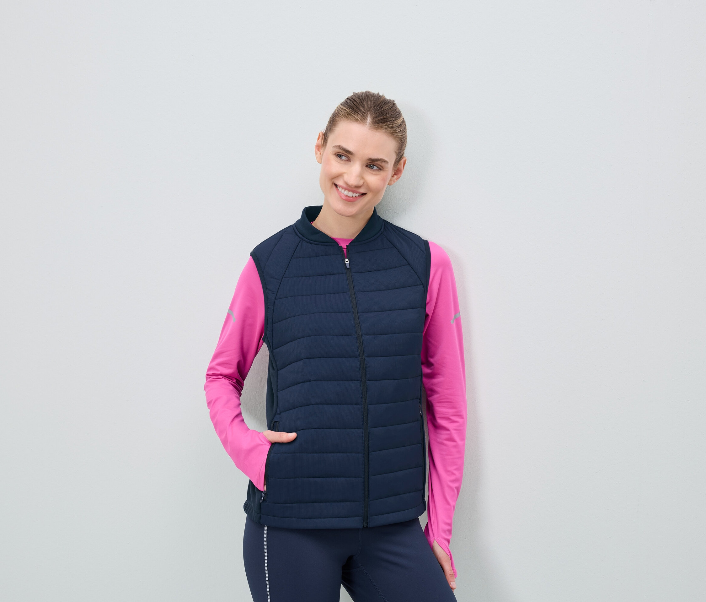 Žena v tmavě modré prošívané vestě a růžovém topu s dlouhým rukávem.