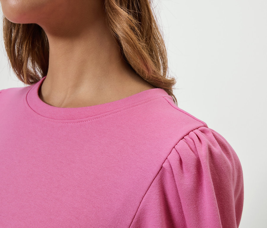 Horní část trupu ženy v růžovém tričku s nabíranými krátkými rukávy.