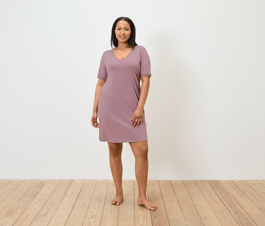 Žena stojí a má na sobě fialové noční šaty s krátkým rukávem.