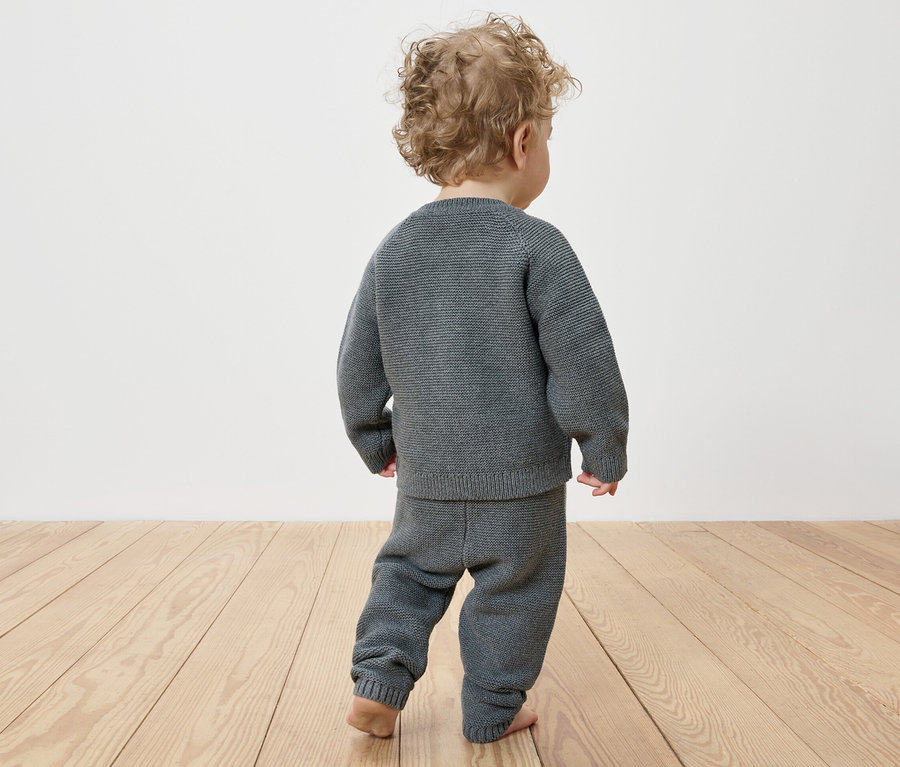 Zezadu je vidět dítě s kudrnatými vlasy, které má na sobě pletenou soupravu.