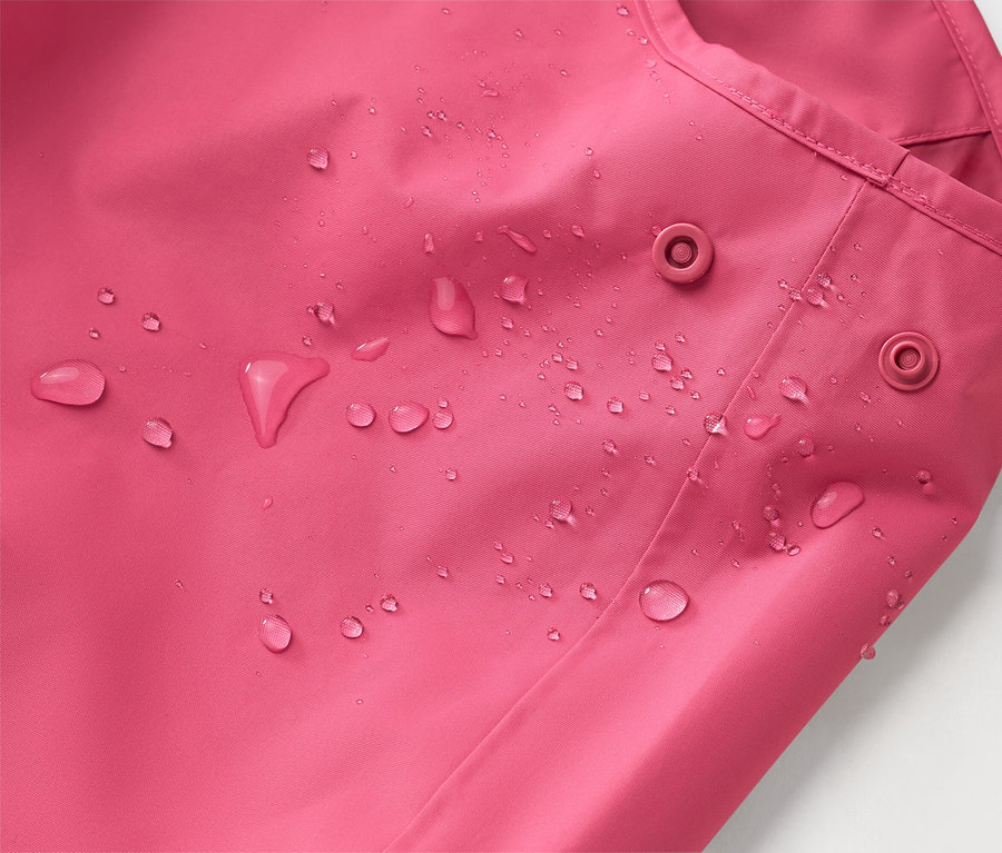 Detail růžové bundy s kapkami vody a dvěma patentkami.