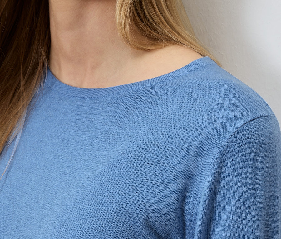 Detailní záběr ženy s blond vlasy ve světle modrém svetru.