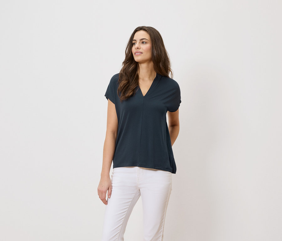 Žena má na sobě tmavě modré tričko a bílé kalhoty na bílém pozadí.