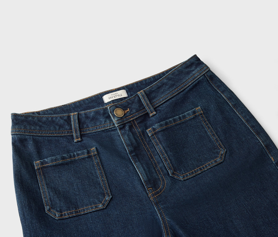 Detail modrých džínů s našitými kapsami a světle hnědým prošíváním.