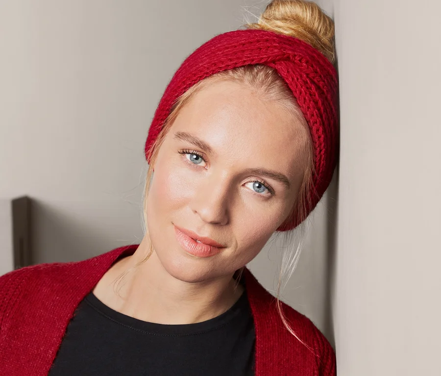 Blondýna se opírá o zeď a má na sobě červenou čelenku.