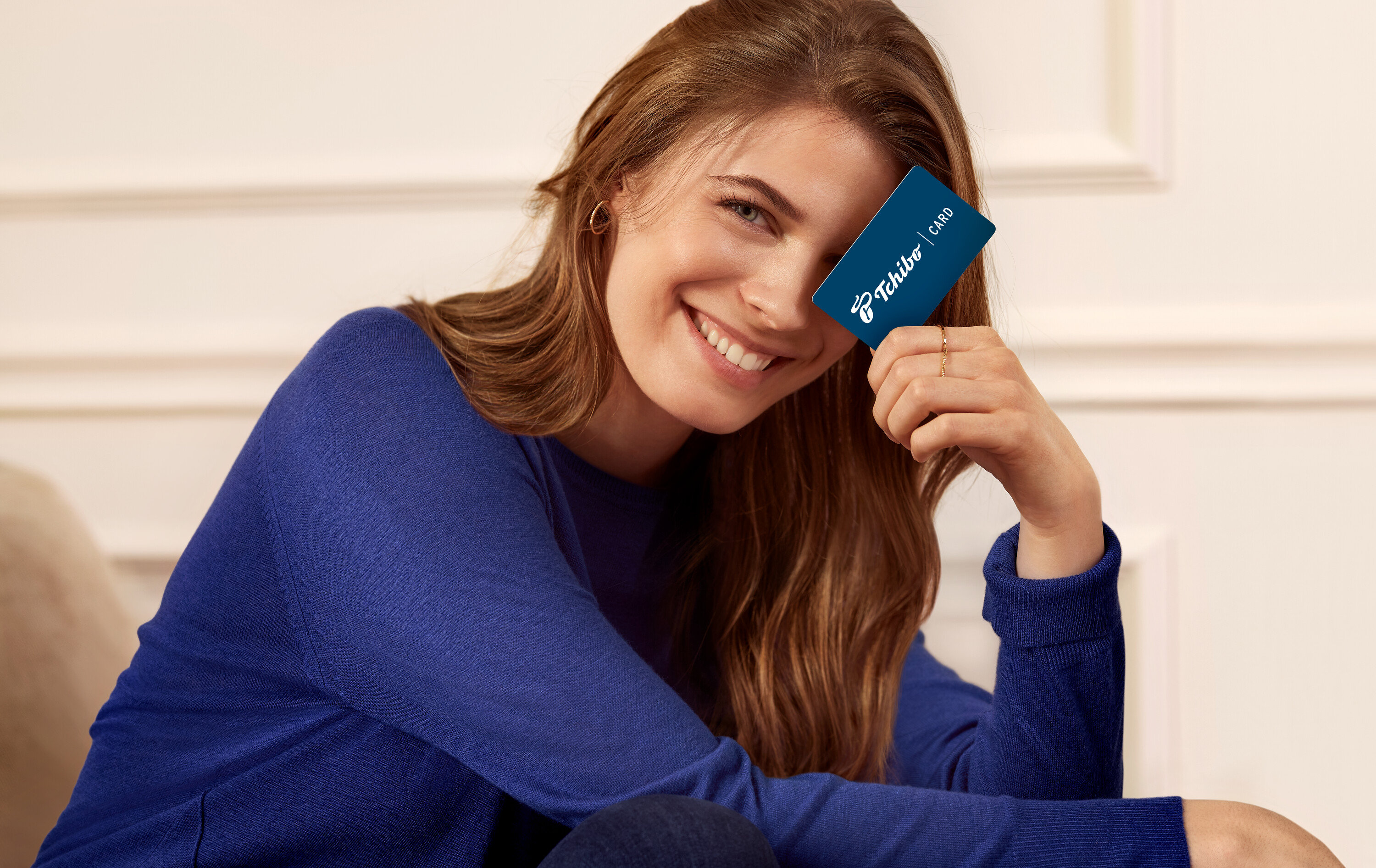 Usmívající se žena drží kartu Tchibo před okem.