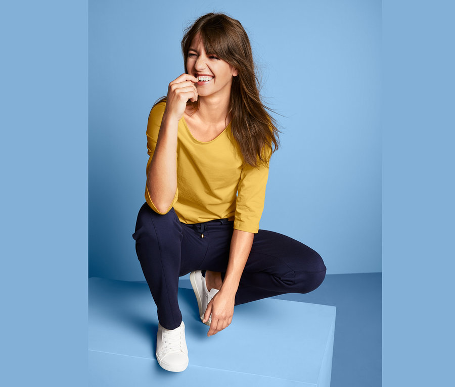 Žena v dřepu se žlutým tričkem s lodičkovým výstřihem.