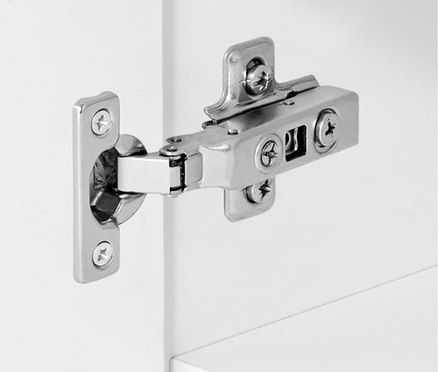 Detail stříbrného pantu na bílé skříňce.