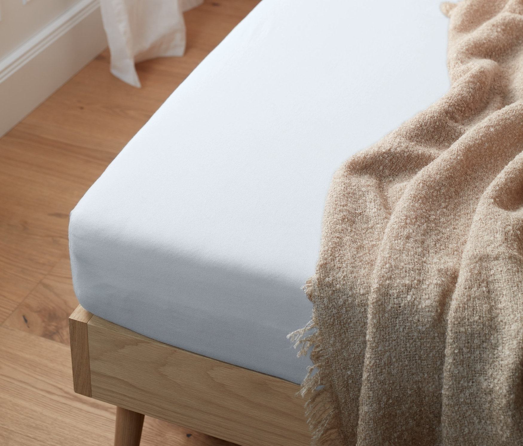 Bílý žerzejové napínací prostěradlo na posteli s béžovou dekou.