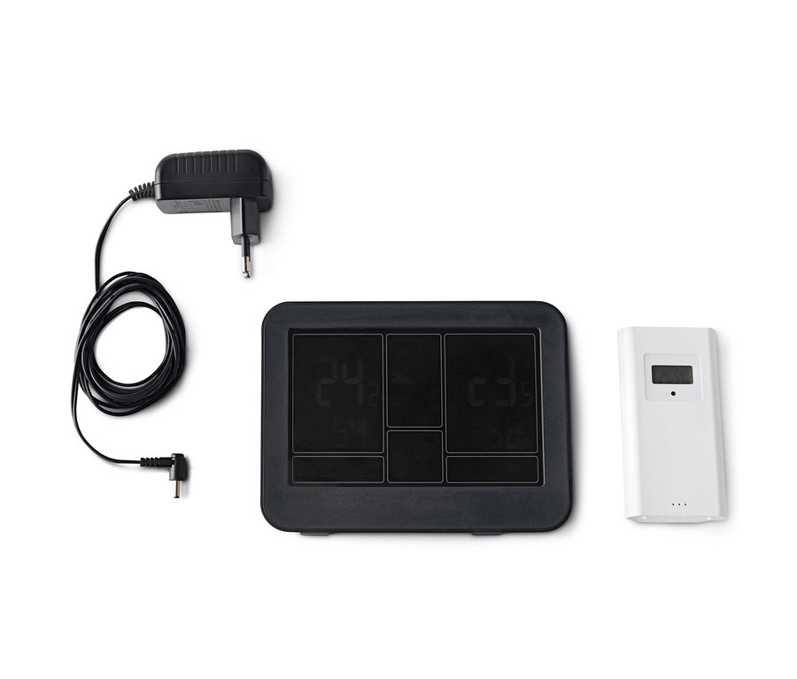 Černá meteostanice s barevným LC displejem, řízená rádiovým signálem, CH, vedle bílého senzoru a adaptéru.